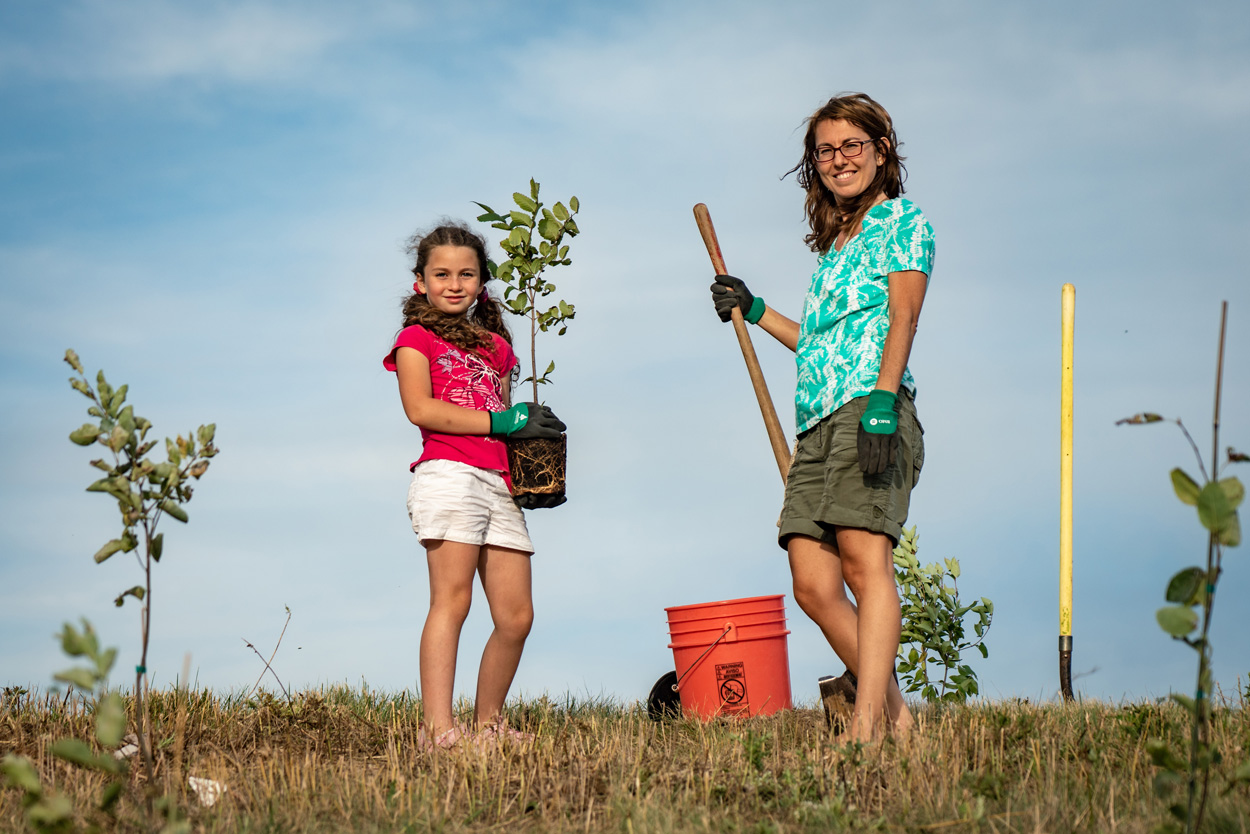 小女孩和妈妈在镜头前摆姿势，一个拿着铲子，另一个拿着小树。